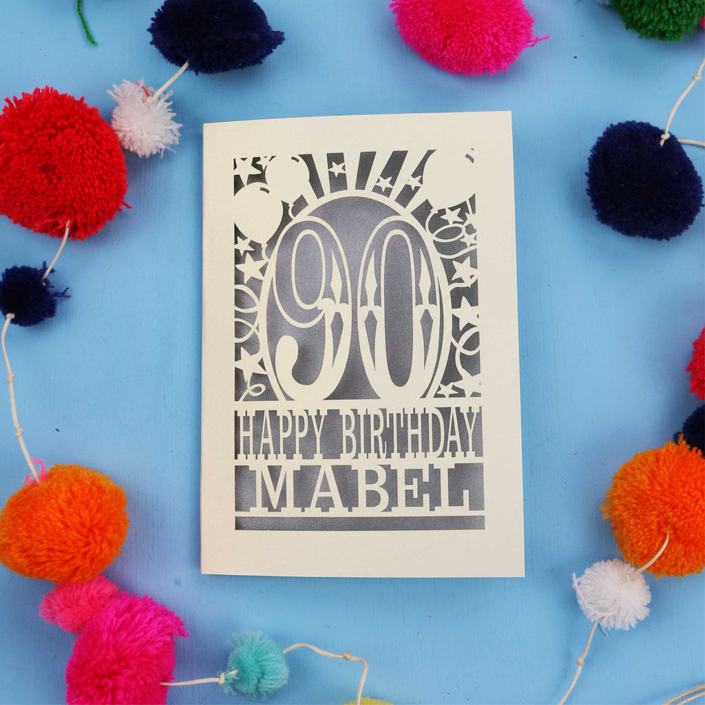 Happy Birthday Mabel - A personalised 90th birthday card with colourful pom-poms on a blue background