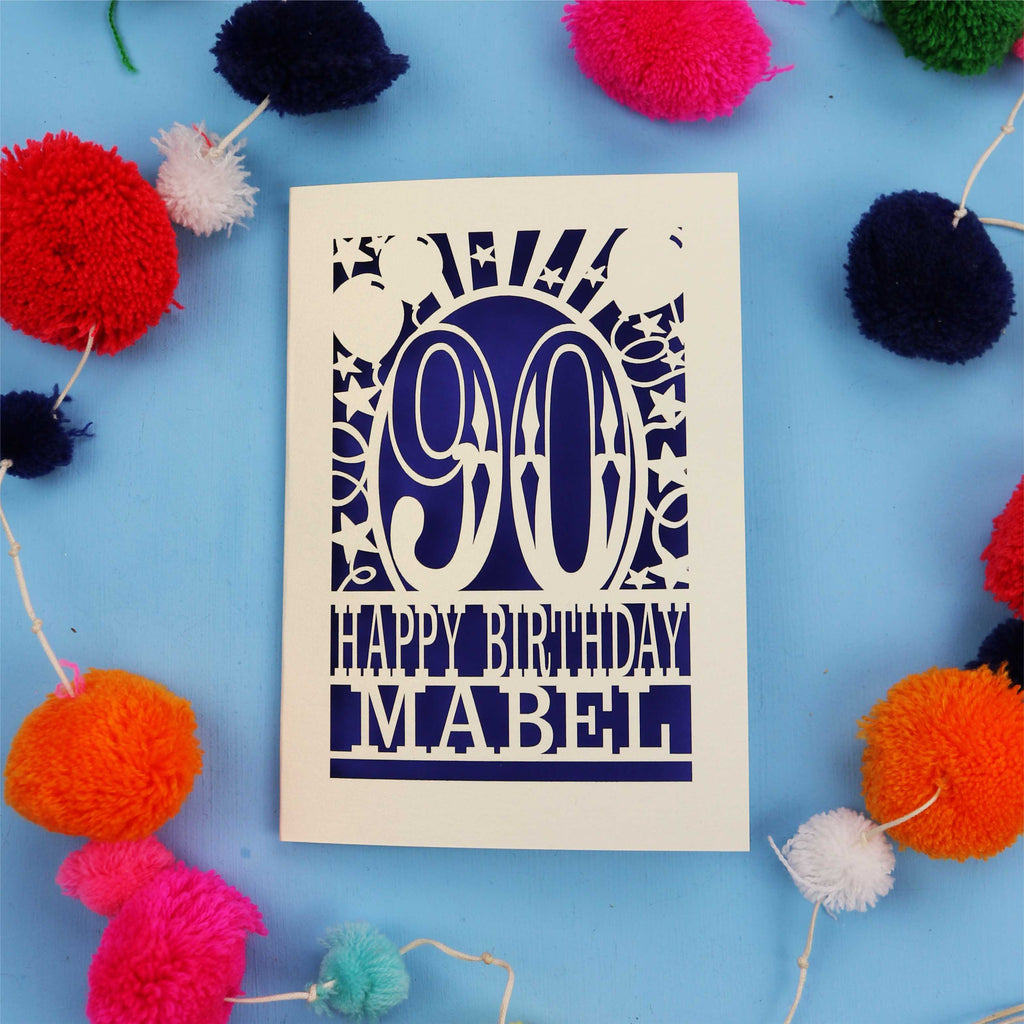Happy Birthday Mabel - A personalised 90th birthday card with colourful pom-poms on a blue background