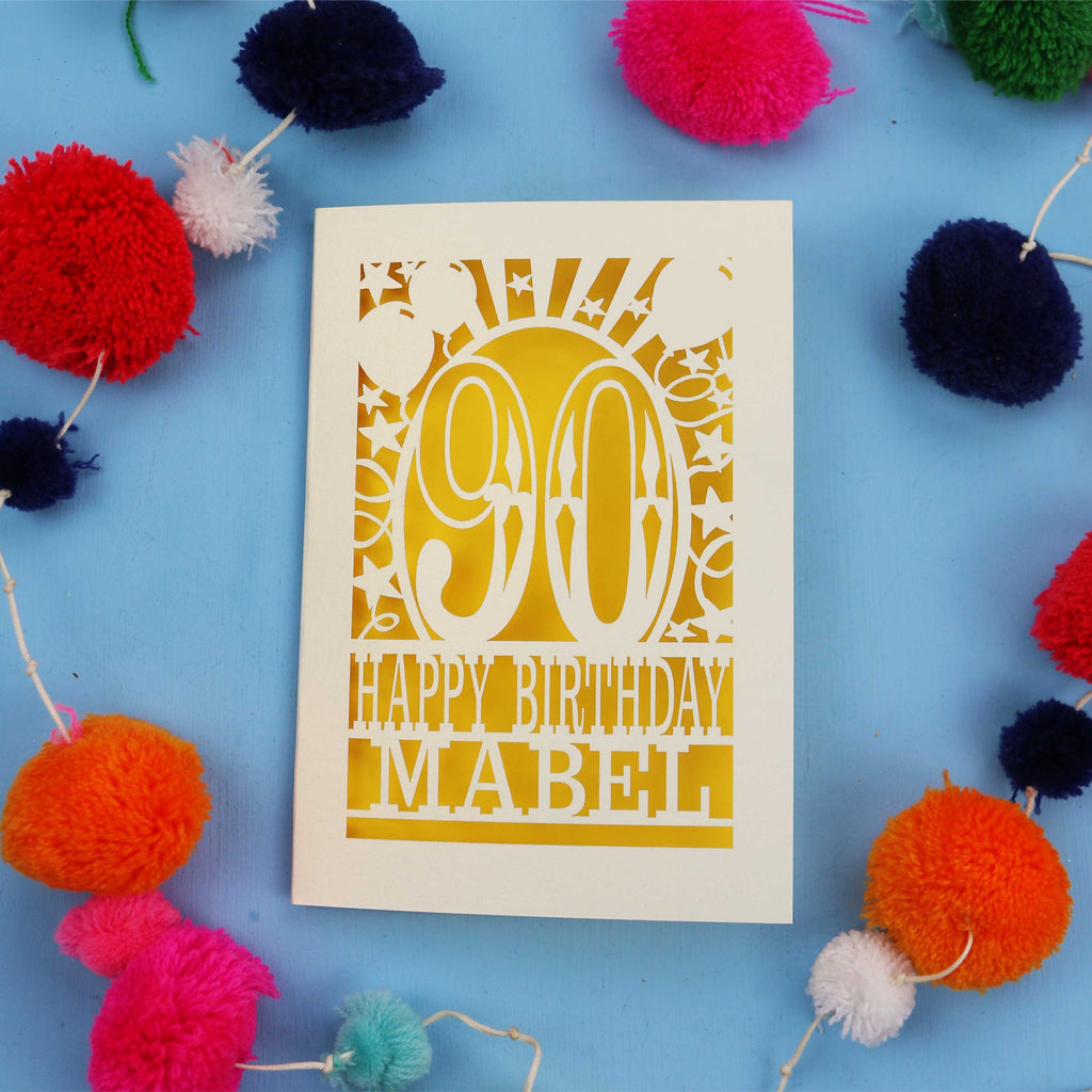 Happy Birthday Mabel - A personalised 90th birthday card with colourful pom-poms on a blue background