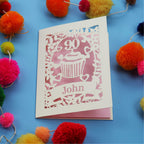 Decorative laser cut 90th birthday card with '90' and 'John' on a blue background with colourful pom-poms.