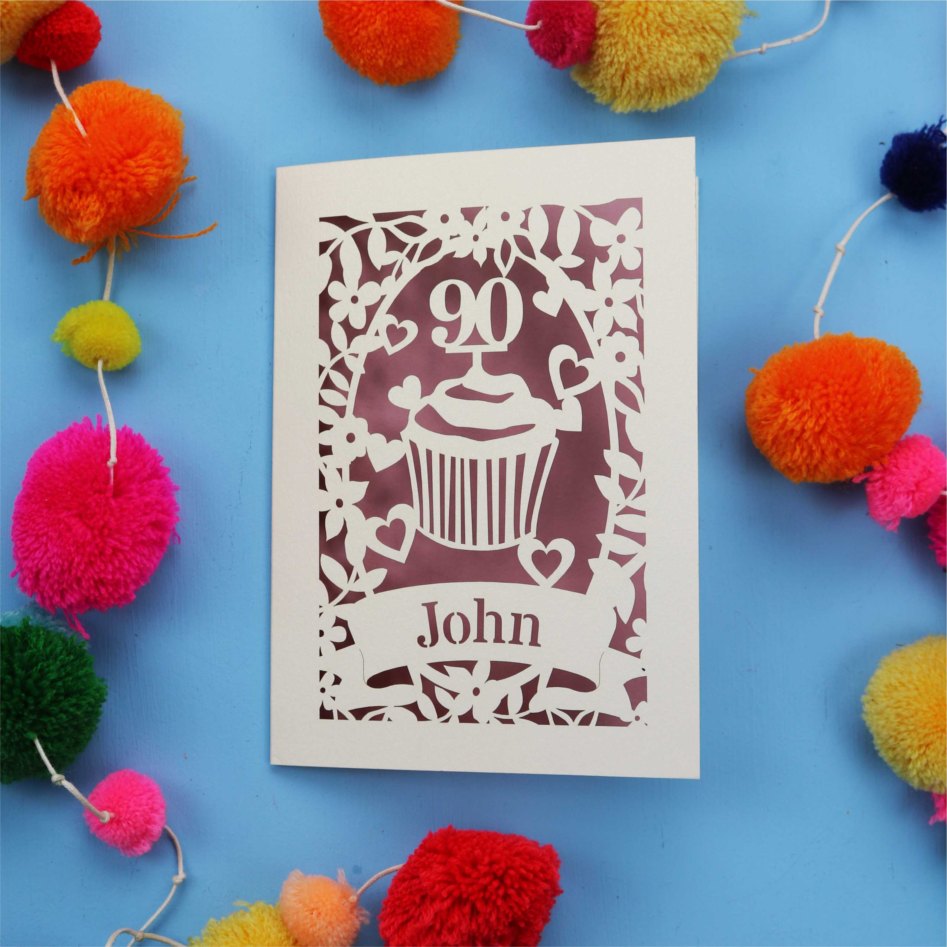 Decorative personalised 90th birthday card with '90' and 'John' on a blue background with colourful pom-poms.