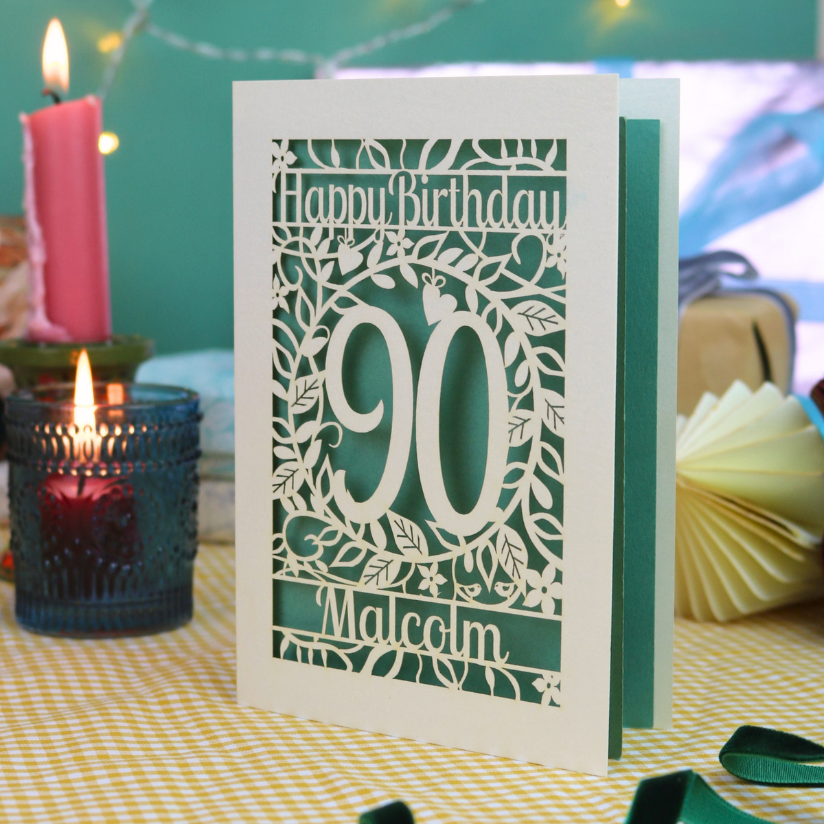A cream laser cut 90th birthday card with leaf border, decorative '90' in the centre and text above, 'Happy Birthday'. The 90th birthday card is personalised at the bottom with the name 'Malcolm'. The birthday card is cream with a sage green paper insert. 