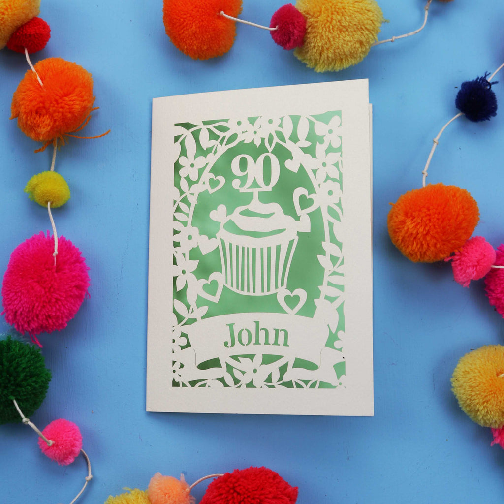 Decorative 90th birthday card with '90' and 'John' on a blue background with colourful pom-poms.