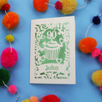 Decorative 90th birthday card with '90' and 'John' on a blue background with colourful pom-poms.