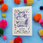 Decorative 90th birthday card with '90' and 'John' on a blue background with colourful pom-poms.