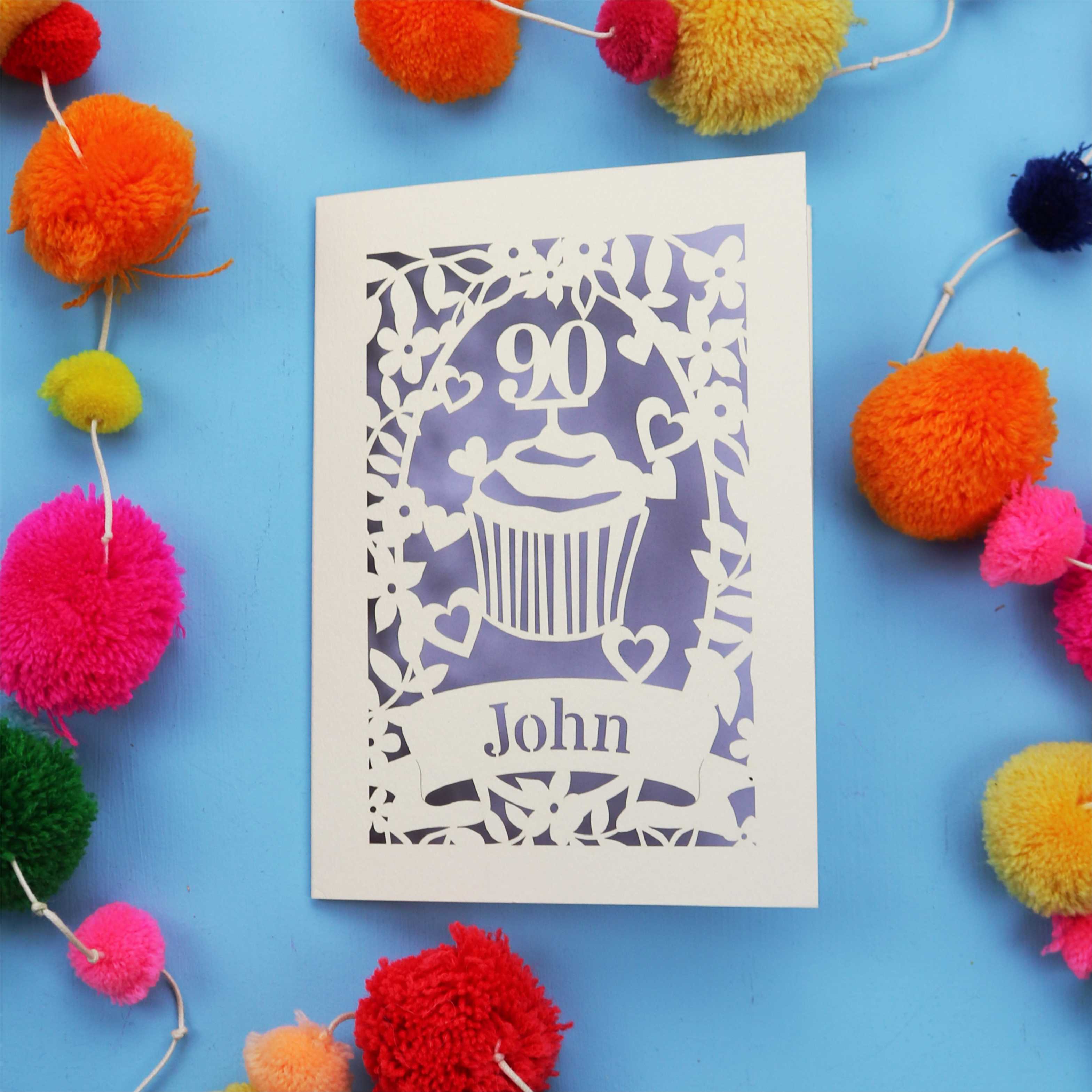 Decorative 90th birthday card with '90' and 'John' on a blue background with colourful pom-poms.