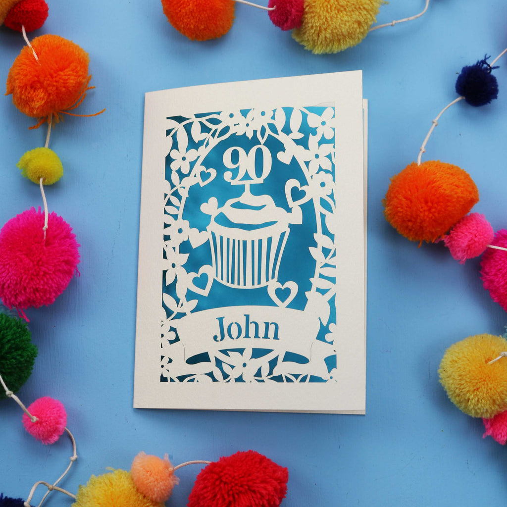Decorative 90th birthday card with '90' and 'John' on a blue background with colourful pom-poms.