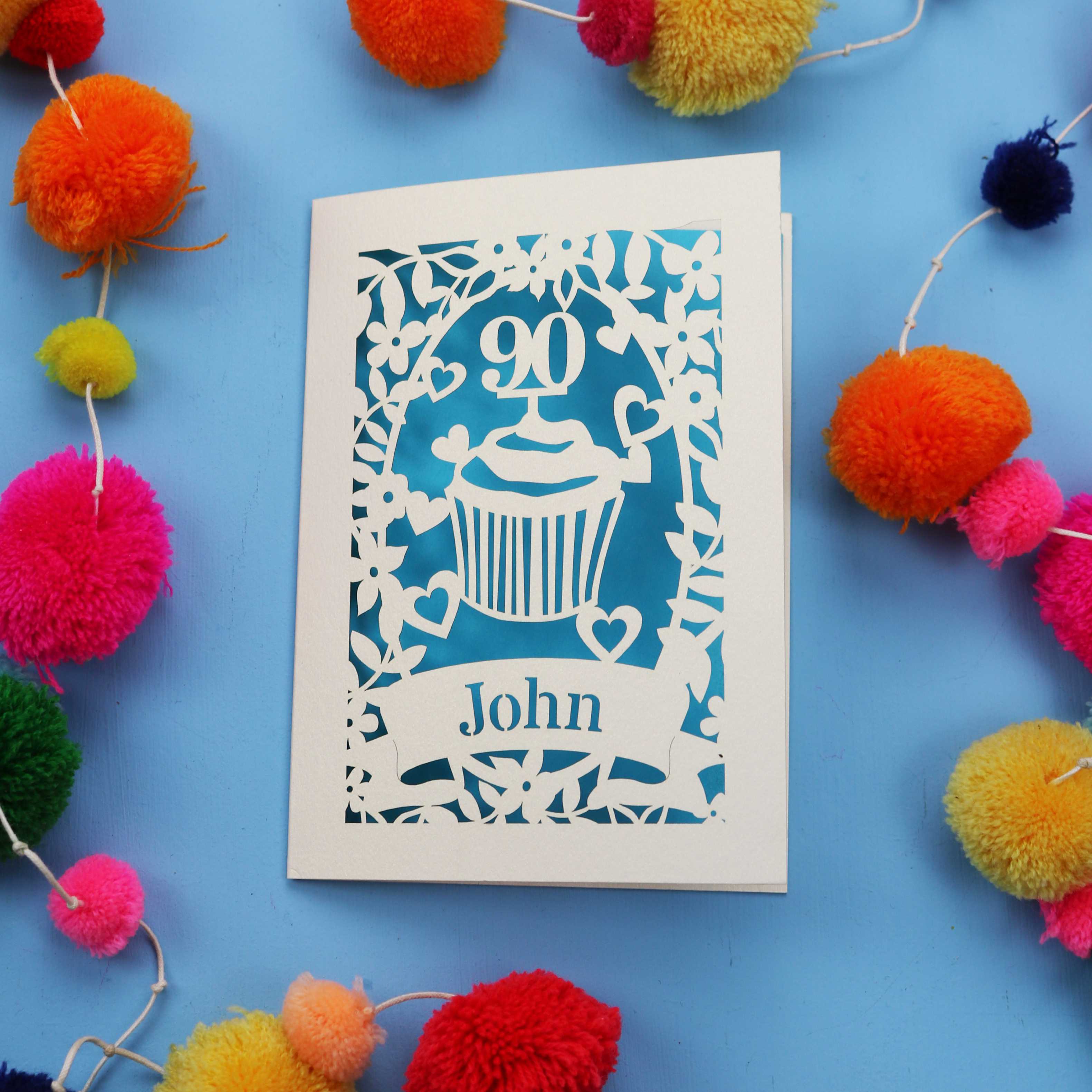 Decorative 90th birthday card with '90' and 'John' on a blue background with colourful pom-poms.