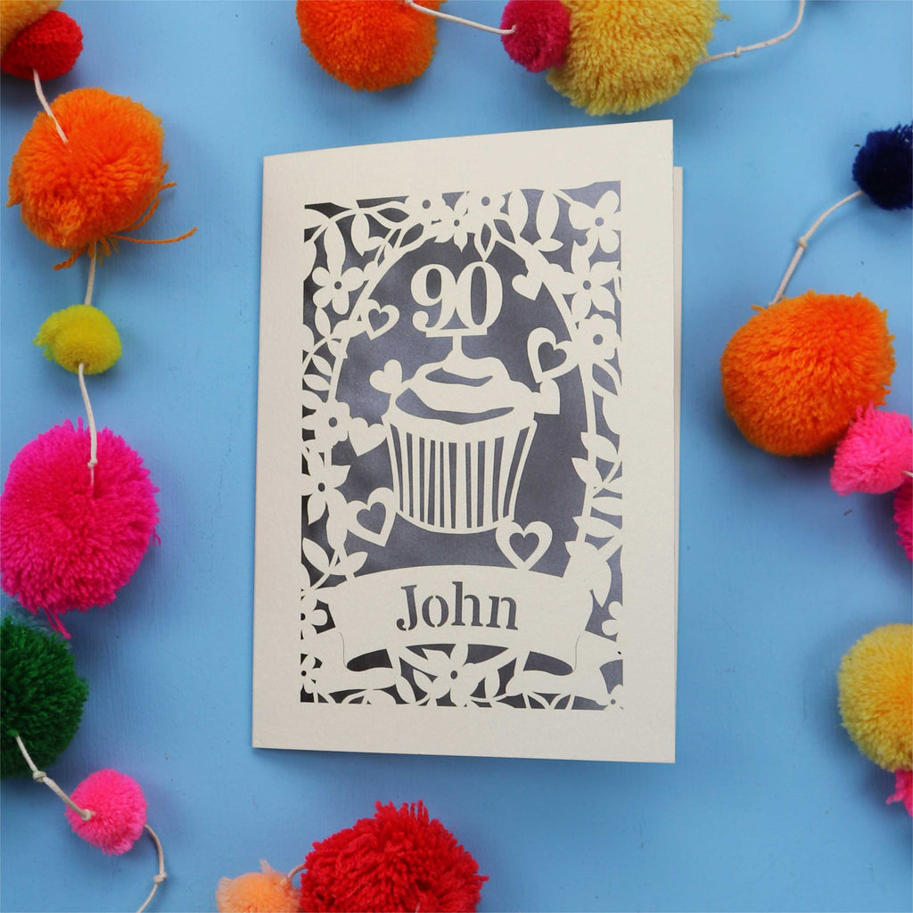 Decorative 90th birthday card with '90' and 'John' on a blue background with colourful pom-poms.