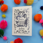 Decorative 90th birthday card with '90' and 'John' on a blue background with colourful pom-poms.