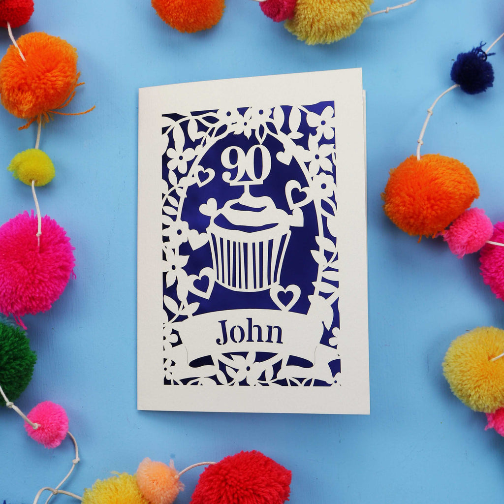 Decorative 90th birthday card with '90' and 'John' on a blue background with colourful pom-poms.