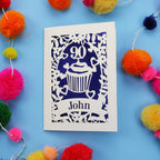Decorative 90th birthday card with '90' and 'John' on a blue background with colourful pom-poms.