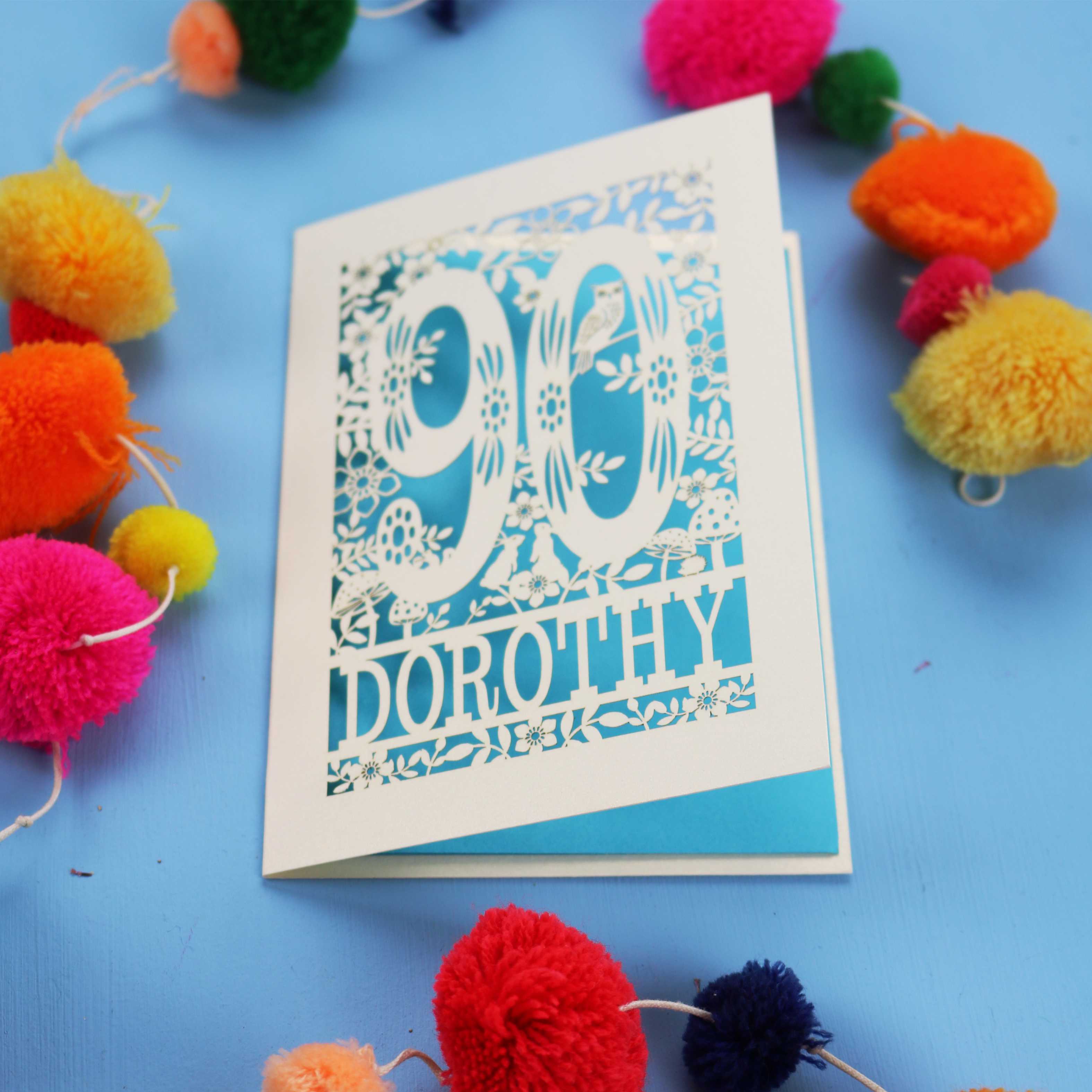 90th Birthday Card with '90 Dorothy' design on a blue background with colourful pom-poms.