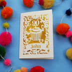 Decorative 90th birthday card with '90' and 'John' on a blue background with colourful pom-poms.