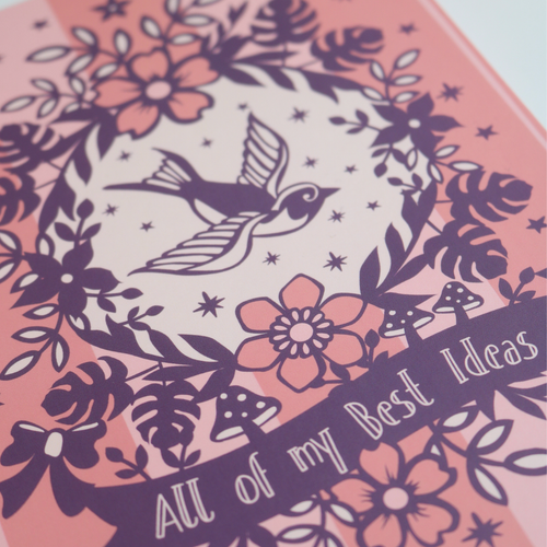 A pink A5 notebook with purple illustrations including a bird and flowers, and text "All of my Best Ideas"