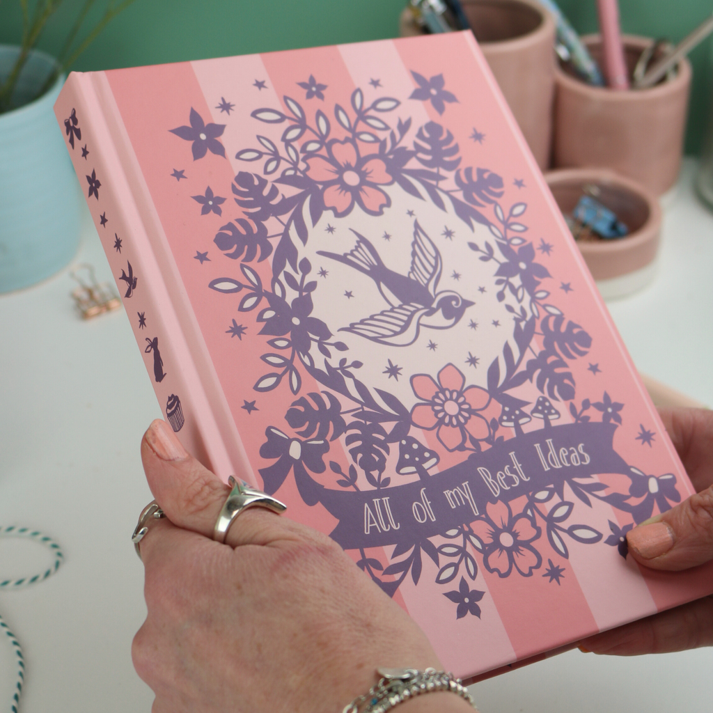 Pink notebook with floral and bird design held by a hand