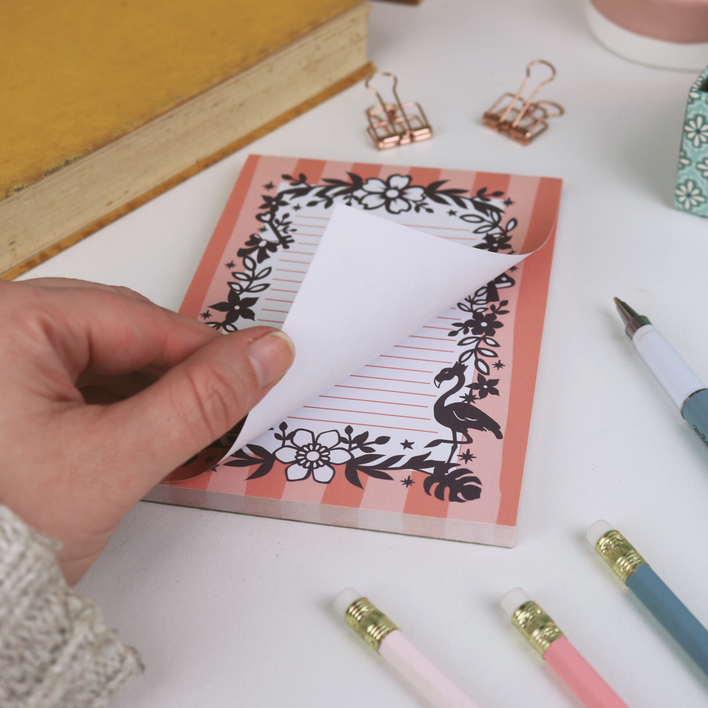 Hand holding a small notebook with decorative cover on a desk with stationery items.