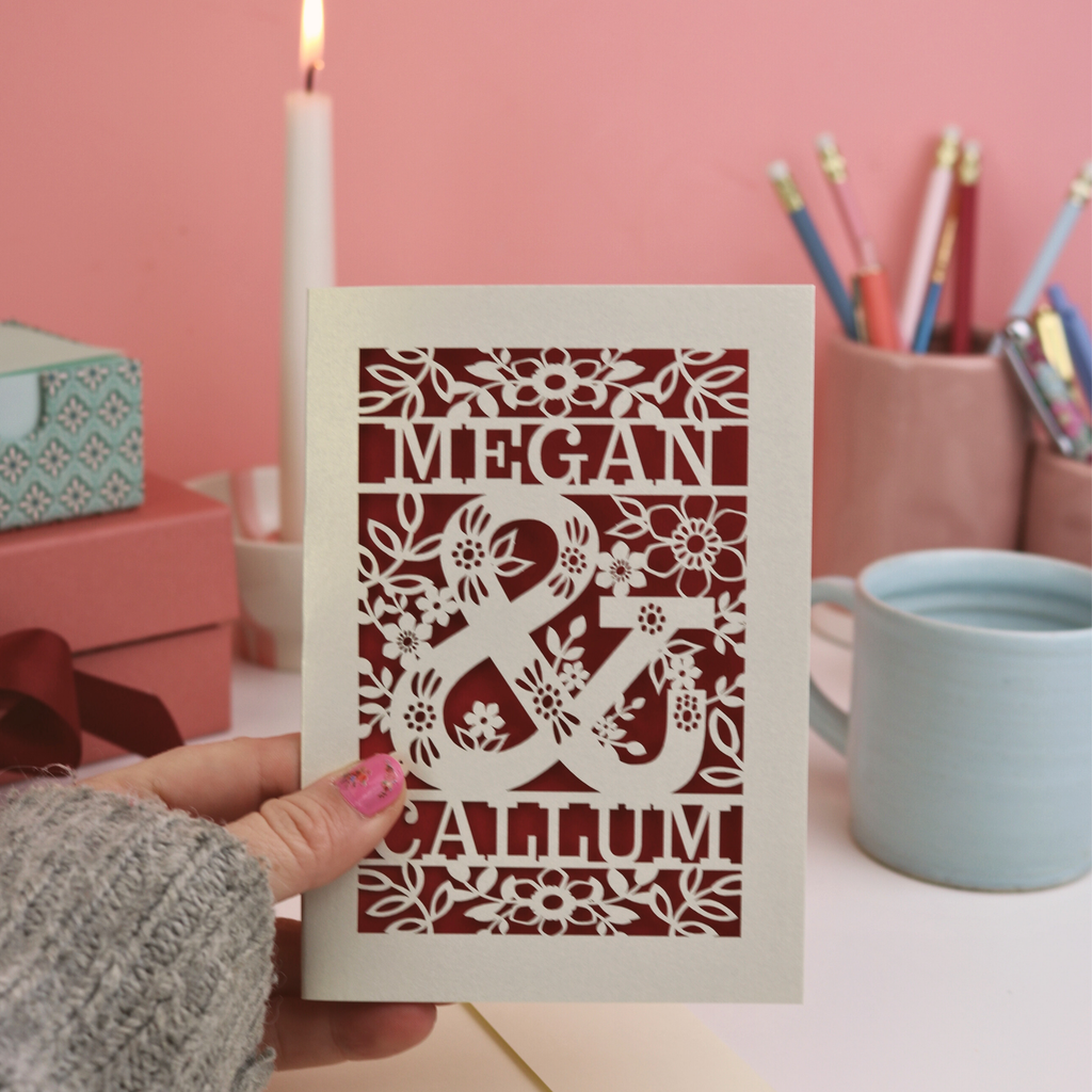 Valentine's Card with laser-cut design of 'Megan & Callum' held by a hand against a pink background.