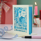 A laser cut Aquarius birthday card personalised with the name Abigail, on a desk with candles and stationery items