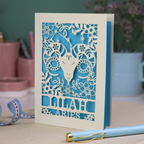 Aries birthday Card with laser-cut design of an Aries symbol and floral elements, with a pen and ribbons on a table.