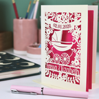 Personalized card with baby pram design and text on a desk with stationery items.