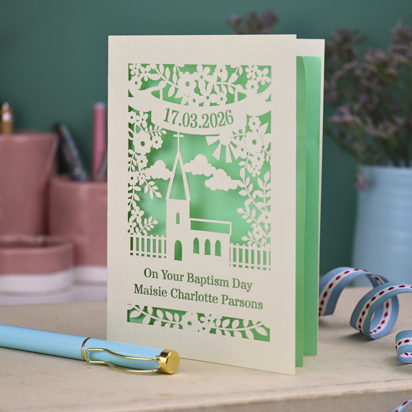 A laser cut Baptism card with floral cut out church design, a banner with cut out date in stencil font and text "On your Baptism Day, Maisie Charlotte Parsons"