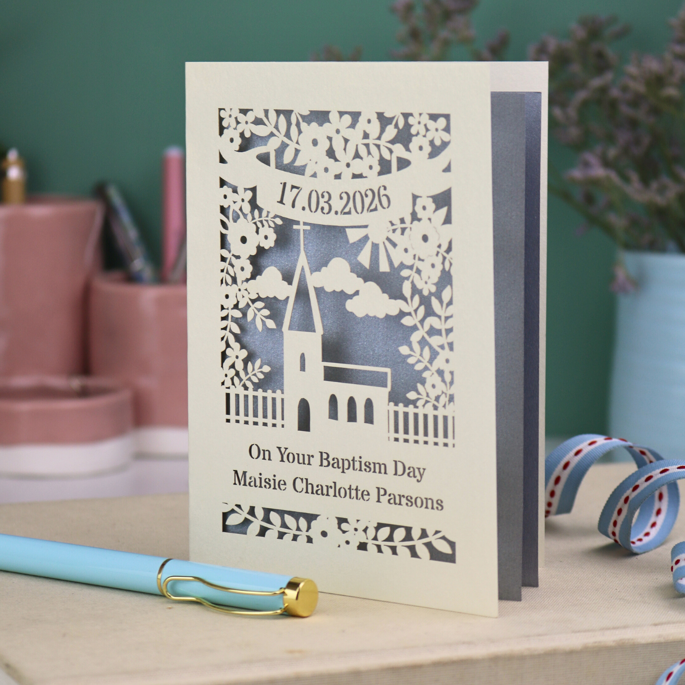 A laser cut Baptism card with floral cut out church design, a banner with cut out date in stencil font and text "On your Baptism Day, Maisie Charlotte Parsons"