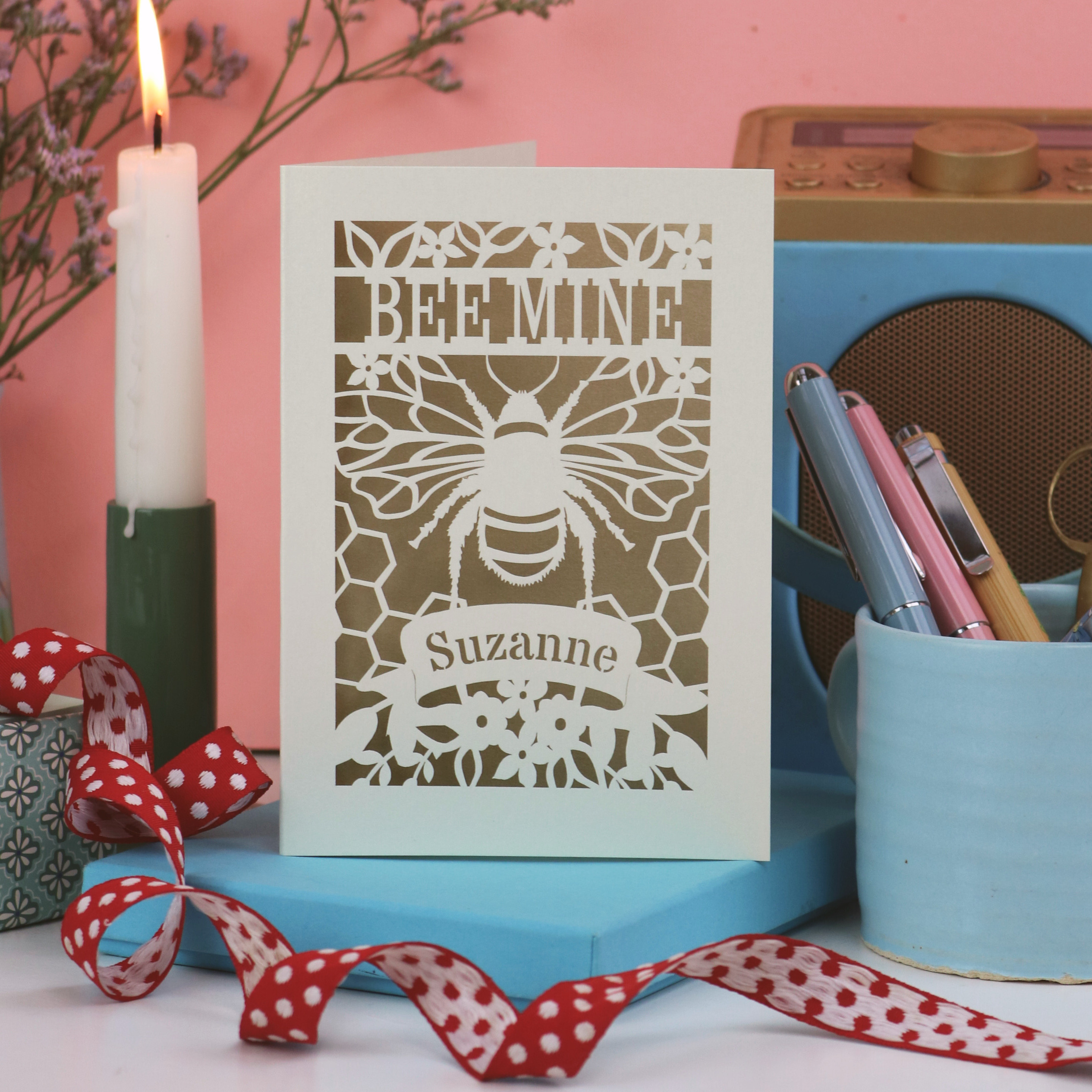 Laser cut Valentine's Card with bee design and 'Bee Mine' text on a pink background with candles and stationery.