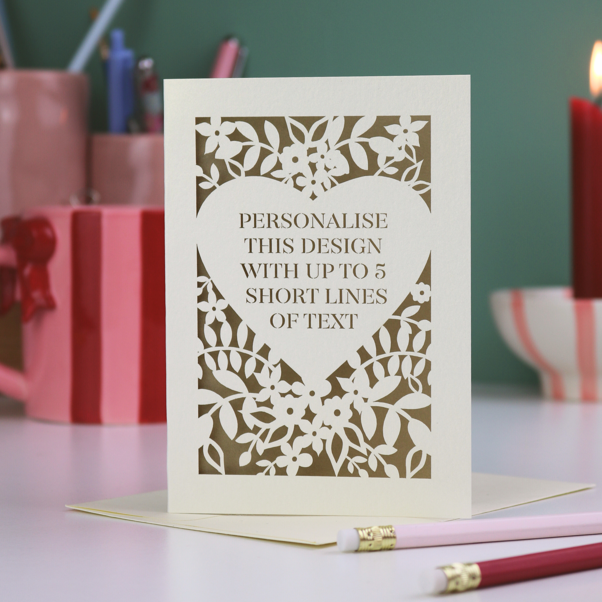 Personalisable laser cut Valentine's card with decorative cut-out design on a table with stationery items.
