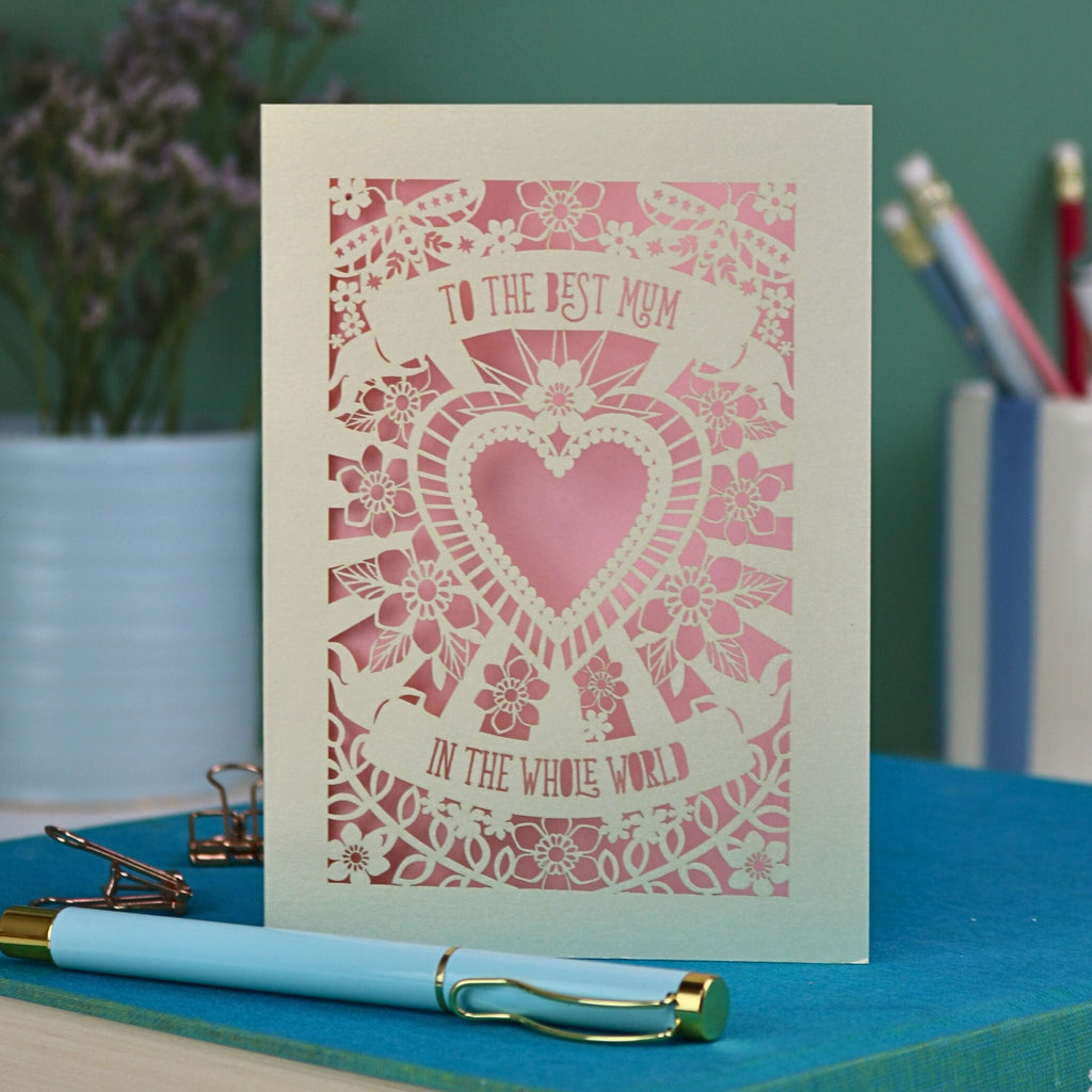 A laser cut Mother's Day card with intricate floral design with heart in the centre and the text "To the best mum in the whole world" cut out of two banners
