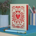 A laser cut card for mum with intricate floral design with heart in the centre and the text "To the best mum in the whole world" cut out of two banners