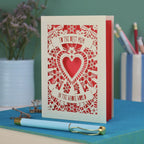 A laser cut card for mum with intricate floral design with heart in the centre and the text "To the best mum in the whole world" cut out of two banners