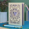 A laser cut card with intricate floral design with heart in the centre and the text "To the best mum in the whole world" cut out of two banners