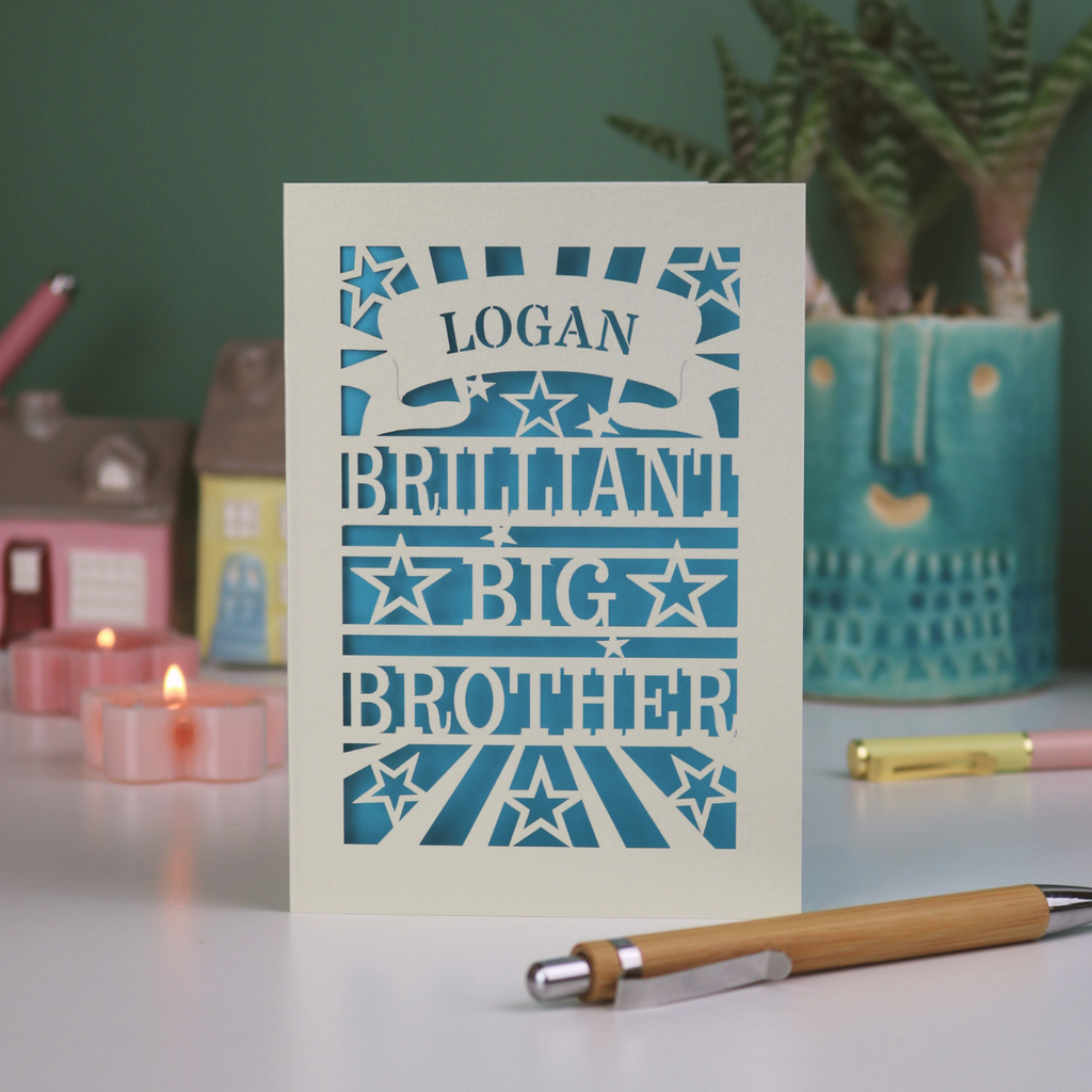 Card with 'Logan, Brilliant Big Brother' text on a table with decorative items.