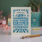 Card with 'Logan, Brilliant Big Brother' text on a table with decorative items.