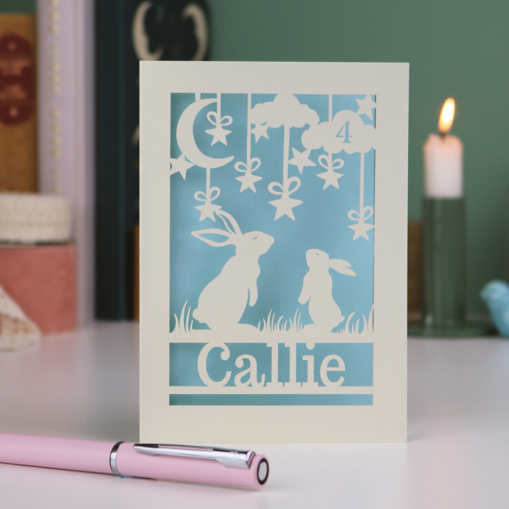 Card with cut-out rabbit design and 'Callie' text on a table with a pen and candle in the background