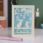 Card with cut-out rabbit design and 'Callie' text on a table with a pen and candle in the background
