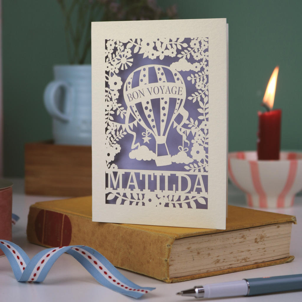 Decorative card with 'Bon Voyage Mathilda' design on a book with a candle and ribbon in the background.