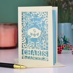 Decorative birthday card with cancer star sign design and 'Charis', 'Cancer' text on a table with a pen and candle.