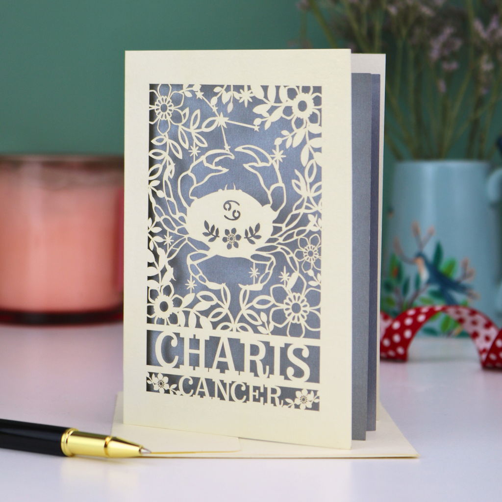 Decorative Cancer birthday card with cancer zodiac design and 'Charis', 'Cancer' text on a table with a pen and candle.