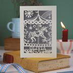 Decorative keepsake birthday card with unicorn carousel design and personalised with a name, standing on a book with a blurred background
