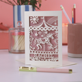 A laser cut greetings card with carousel design, on white desk with stationery items