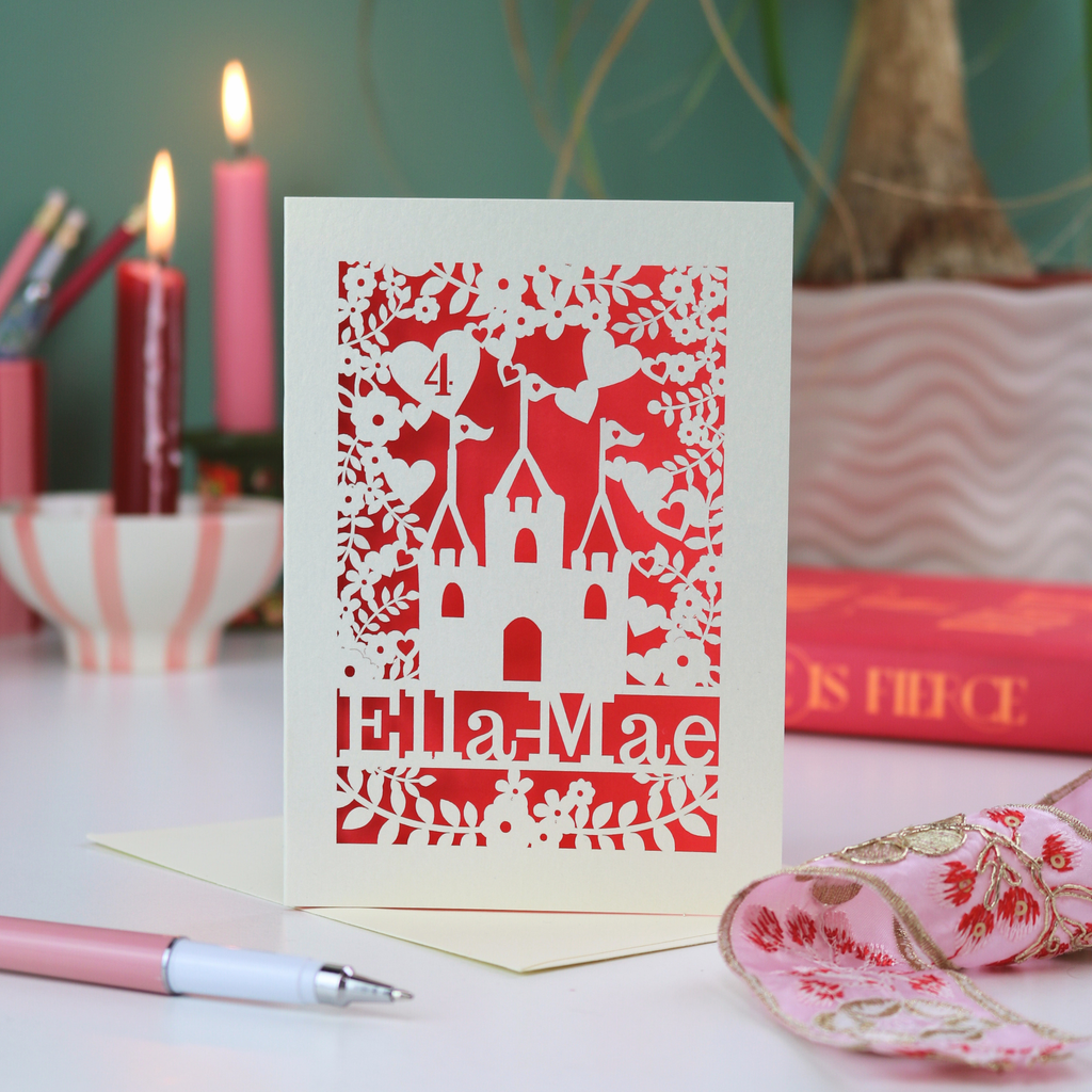 Papercut birthday Card with castle design and 'Ella Mae' text on a table with candles and books.