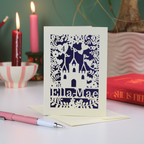 Decorative castle birthday  card with cut-out design and 'Ella Mae' text, placed on a white surface with candles and books in the background.