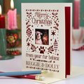 A personalized pet Christmas card with a photo of two dogs, printed with 'Merry Christmas from your fur babies REGGIE & DOLLY' in dark red. The card is shown standing open on a table with a pencil resting in front, with blurred holiday candles in the background.