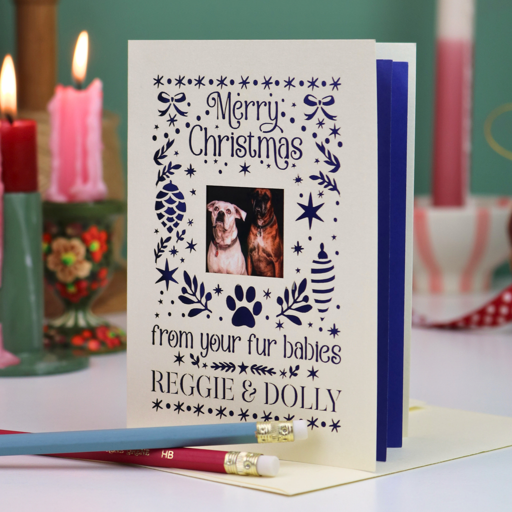 A personalized Christmas greeting card with a photo of two dogs, displayed on a table with candles in the background.
