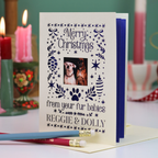 A personalized Christmas greeting card with a photo of two dogs, displayed on a table with candles in the background.