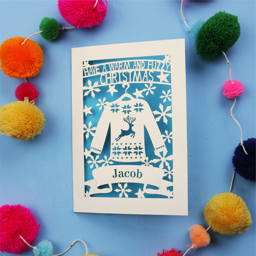 Unique Christmas card with festive Christmas jumper design on a blue background with colourful pom-poms.