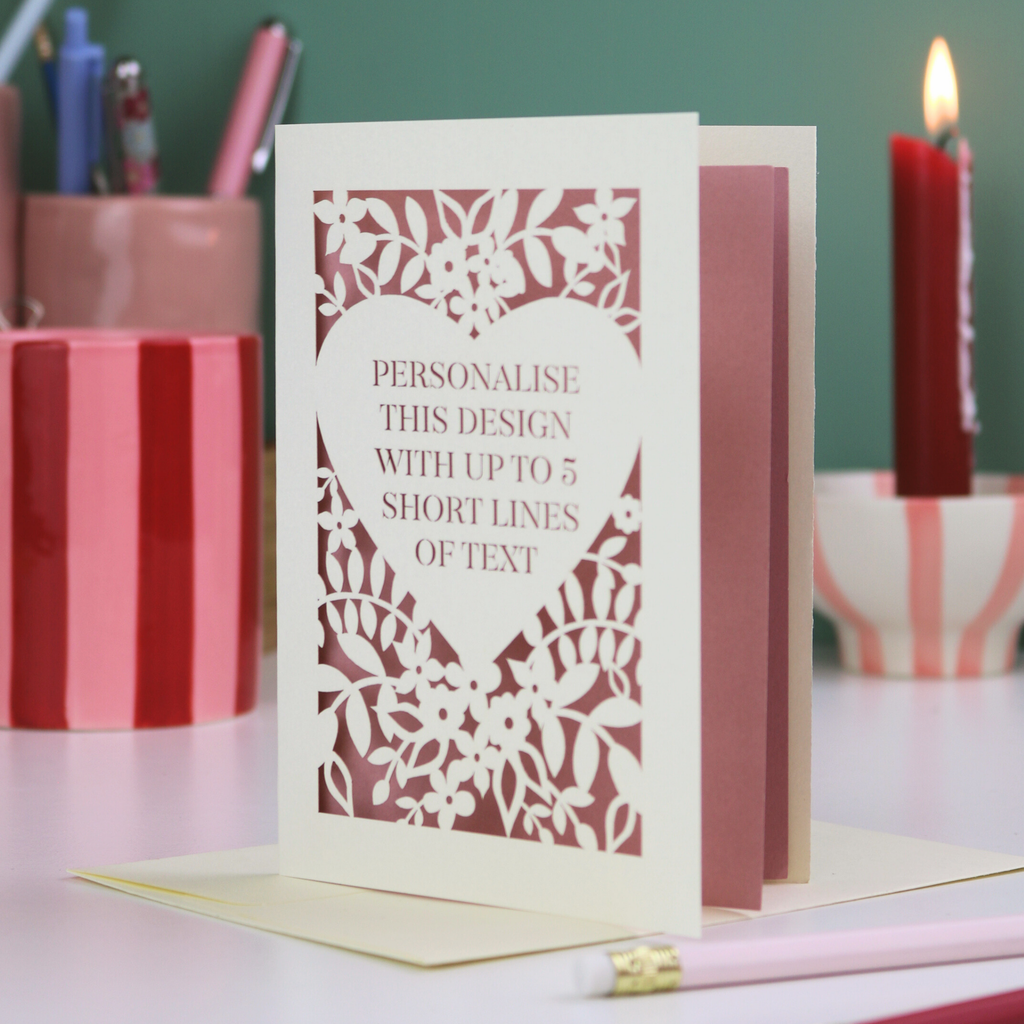 Personalisable card with decorative cut-out design on a table with stationery items.