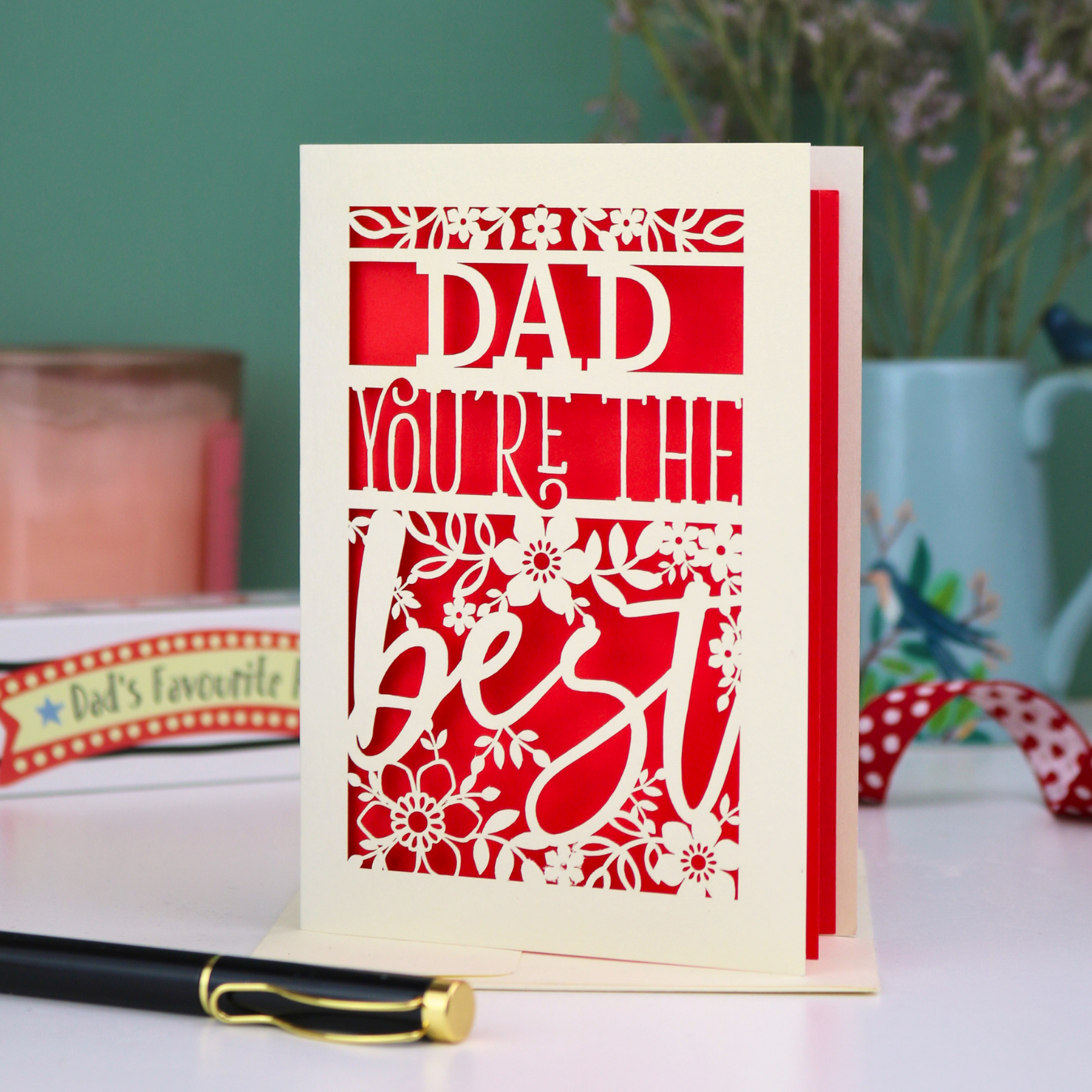 Laser cut Father's Day Card with 'Dad, you're the best' text on a table with decorative items in the background